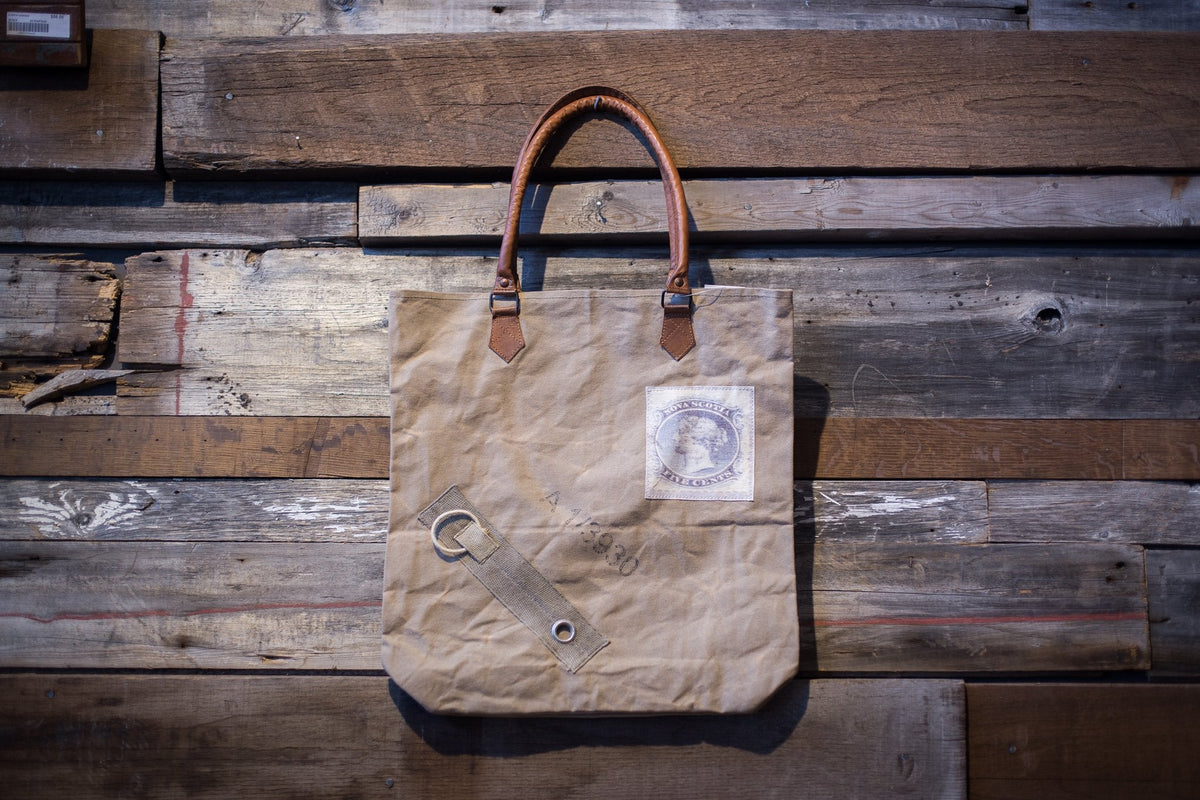 Sac en toile à anses de cuir et petite étiquette cousue, sur un mur de planches