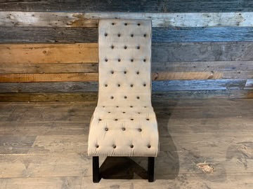 Fauteuil Bibo capitonné en toile beige vu de face, devant un mur de planches