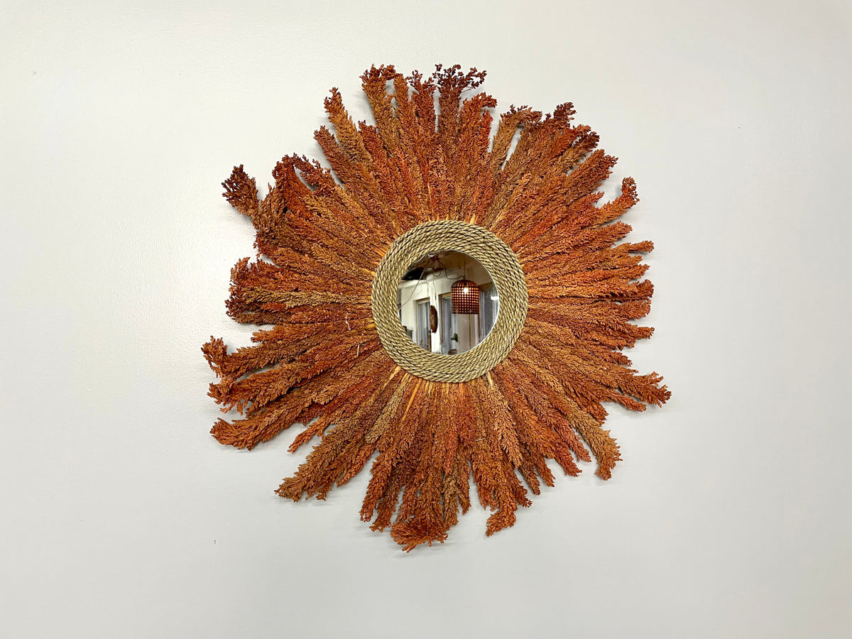 Miroir soleil en rotin et feuilles séchées orangées, vu de face