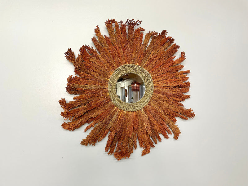 Miroir soleil en rotin et feuilles séchées orangées, vu de face